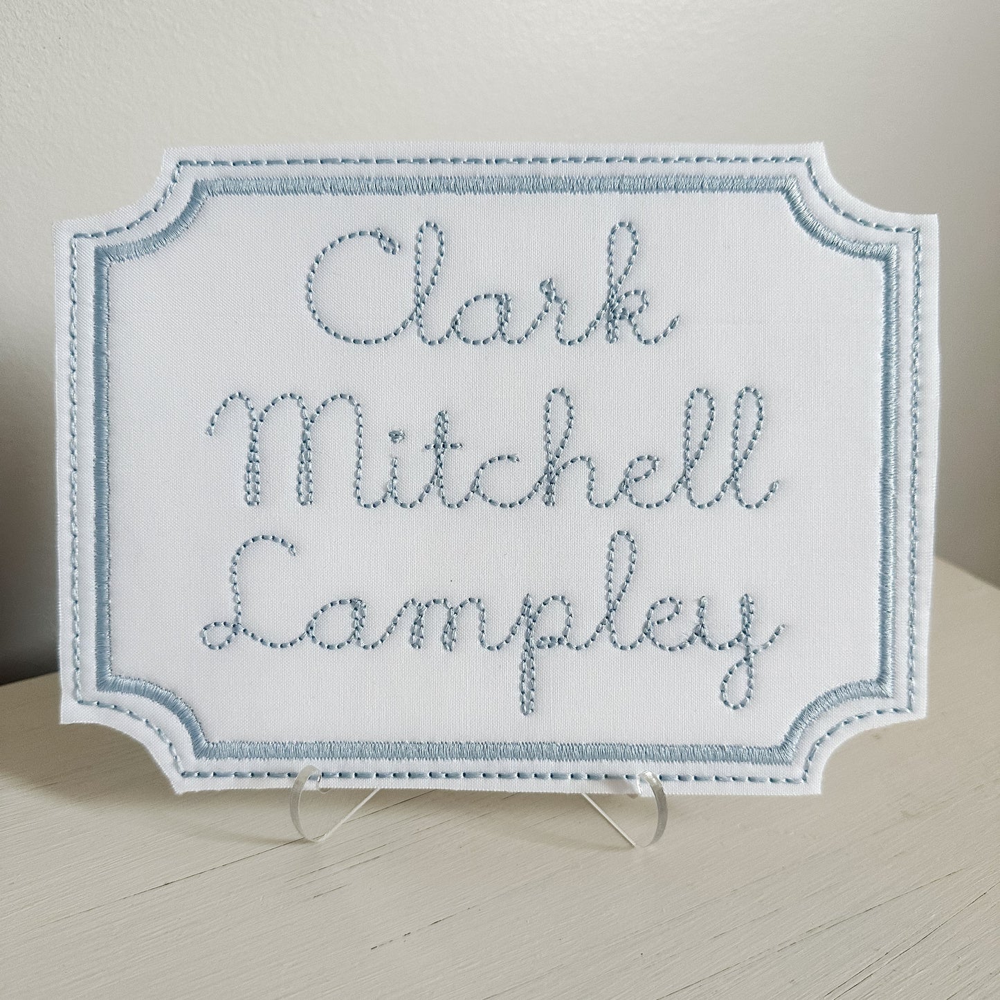 Embroidered nameplate with 'Clark Mitchell Lampley' on a stand against a neutral background. Customize this nameplate with the name of your choosing.