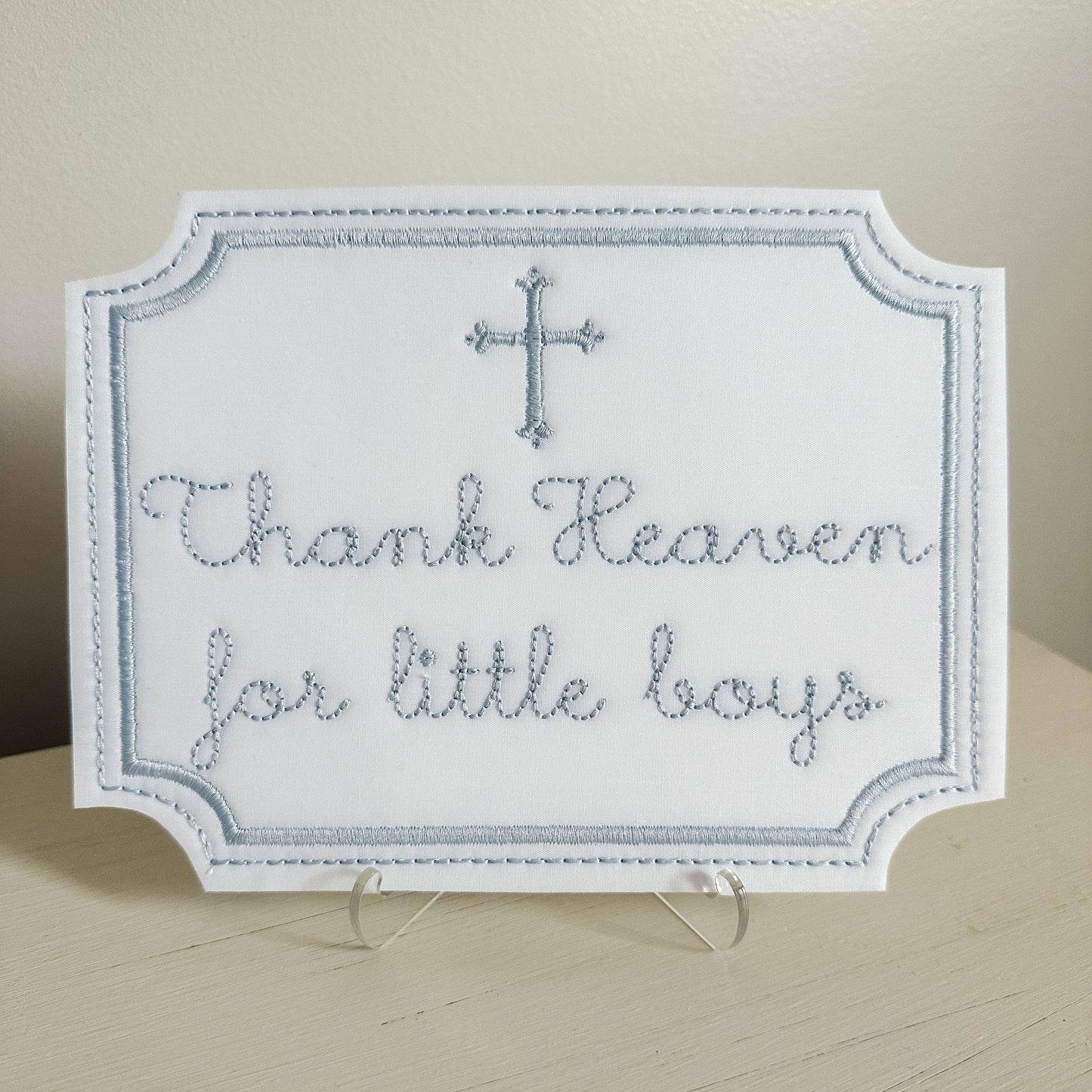 Decorative sign with 'Thank Heaven for little boys' text and a cross on a stand.