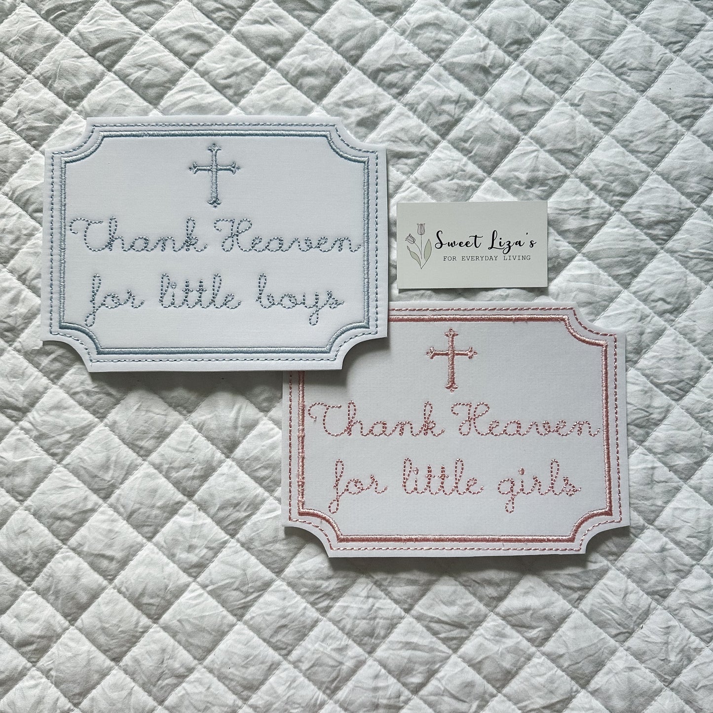 Two embroidered cards on a quilted fabric background with text 'Thank Heaven for little boys' and 'Thank Heaven for little girls'.