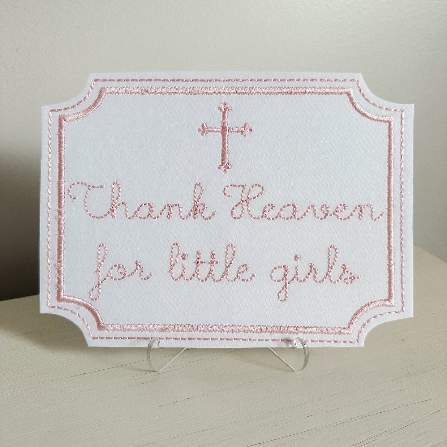 Embroidered sign with 'Thank Heaven for little girls' text on a stand.