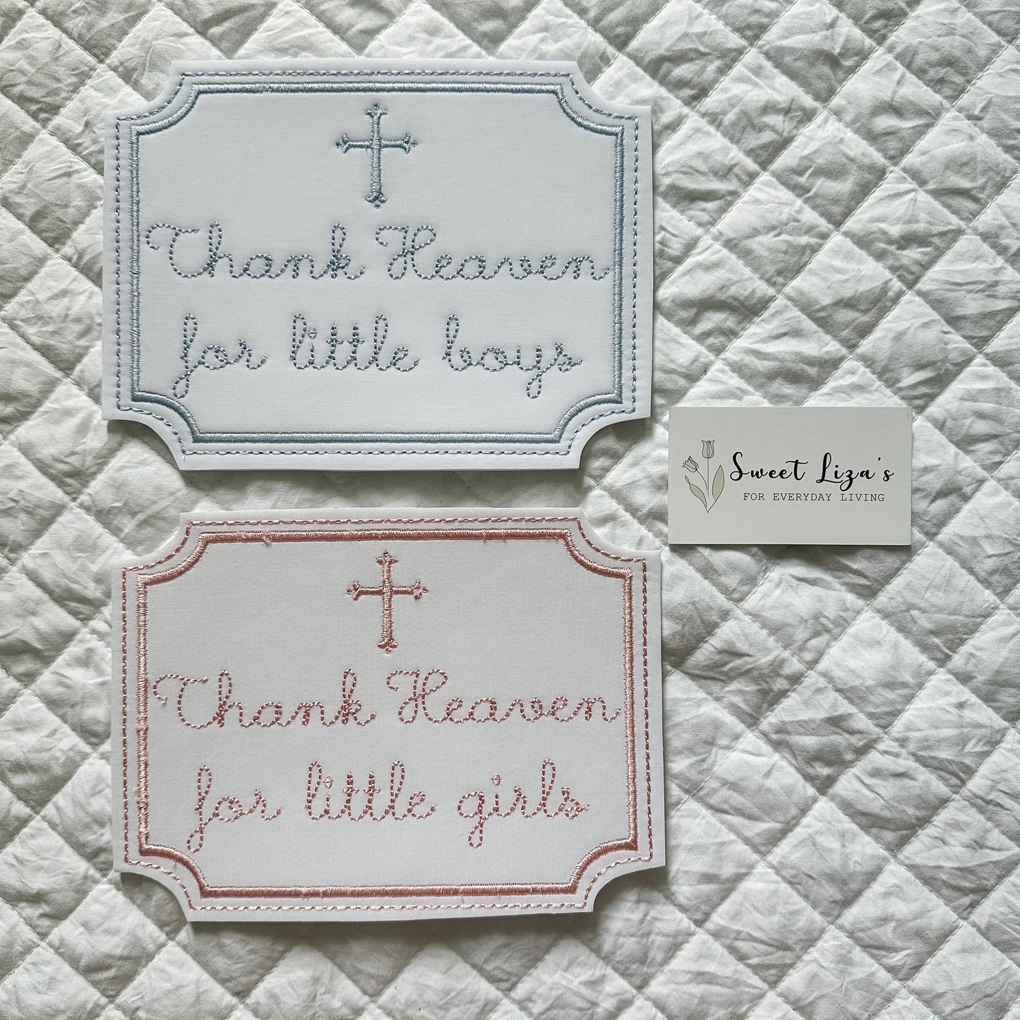 Two embroidered cards on a quilted fabric background, one with 'Thank Heaven for little boys' and the other with 'Thank Heaven for little girls'.