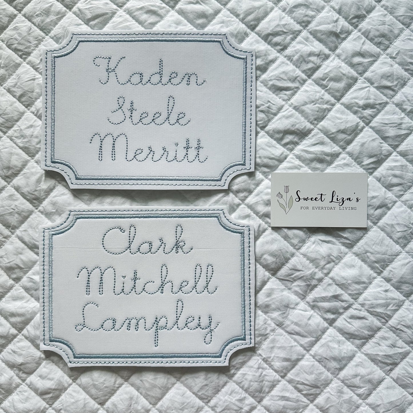 Two embroidered nameplates on a quilted fabric background with 'Sweet Liza's' branding.