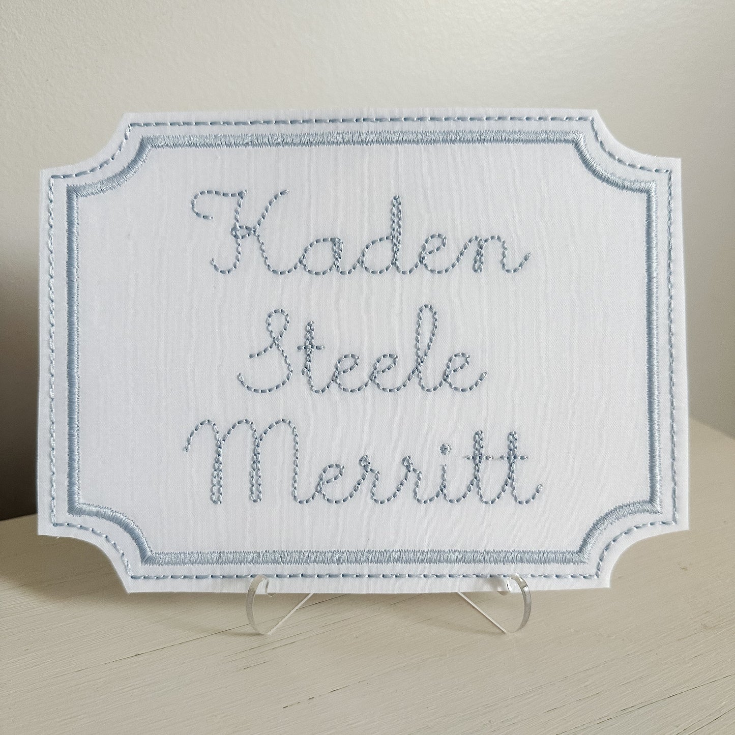 Embroidered nameplate with 'Kaden Steele Merritt' on a stand against a neutral background