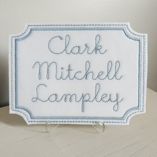 Embroidered nameplate with 'Clark Mitchell Lampley' on a stand against a neutral background. Customize this nameplate with the name of your choosing.