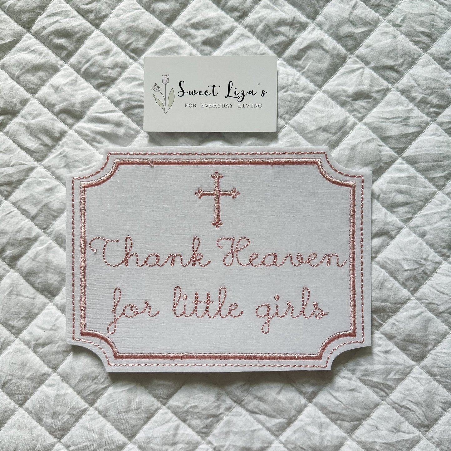 Embroidered sign with 'Thank Heaven for little girls' on a quilted fabric background