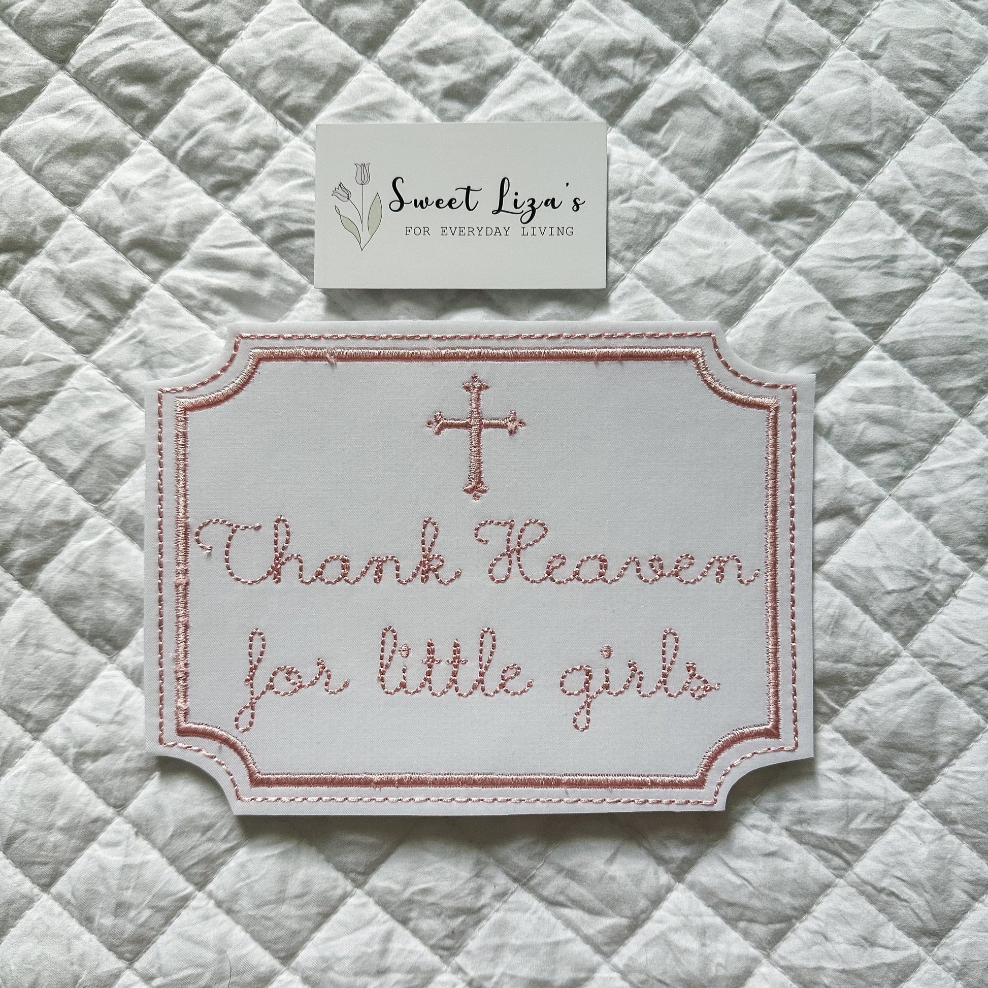 Embroidered sign with 'Thank Heaven for little girls' on a quilted fabric background