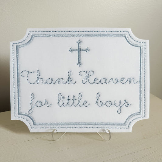Decorative sign with 'Thank Heaven for little boys' text and a cross on a stand.