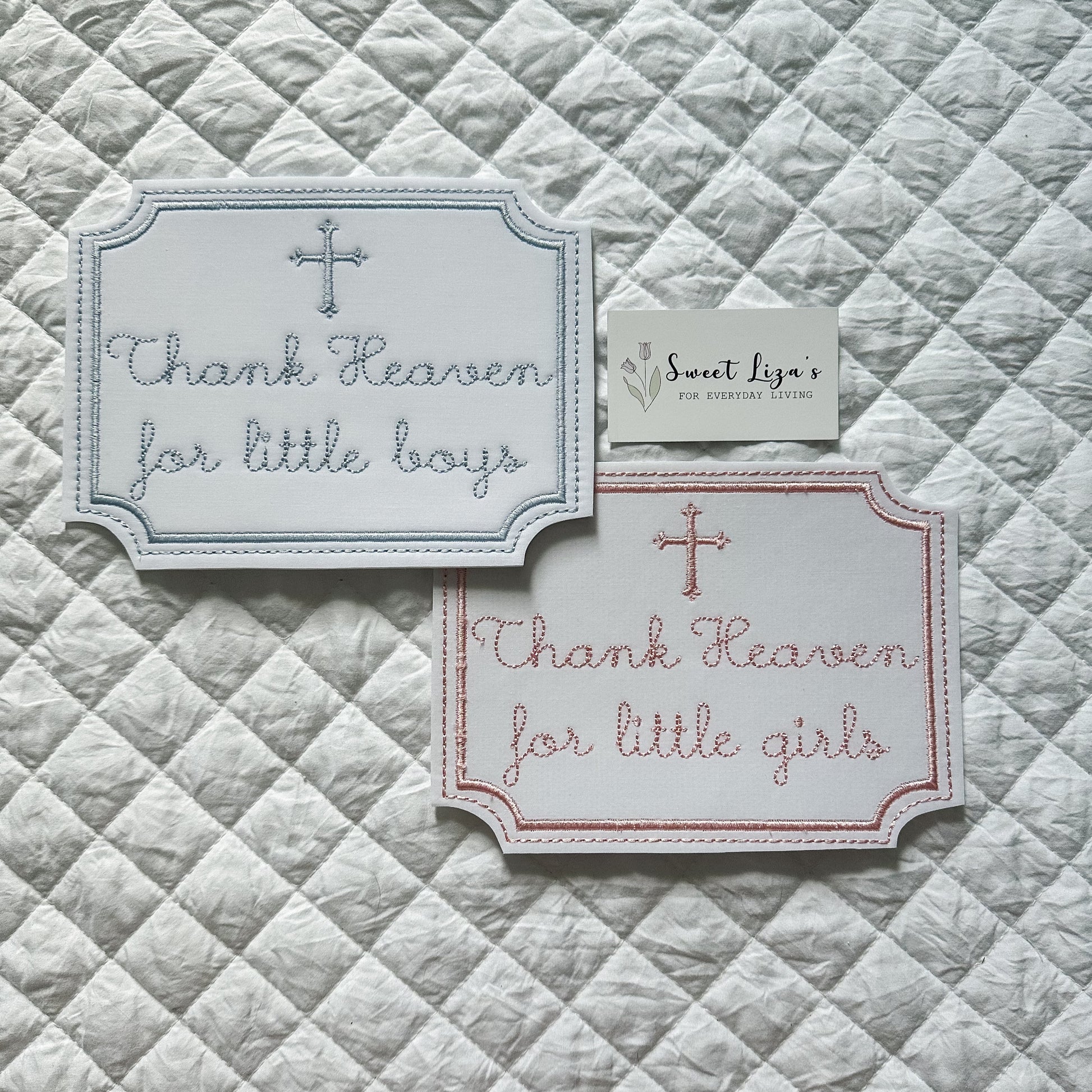 Two embroidered cards on a quilted fabric background with text 'Thank Heaven for little boys' and 'Thank Heaven for little girls'.