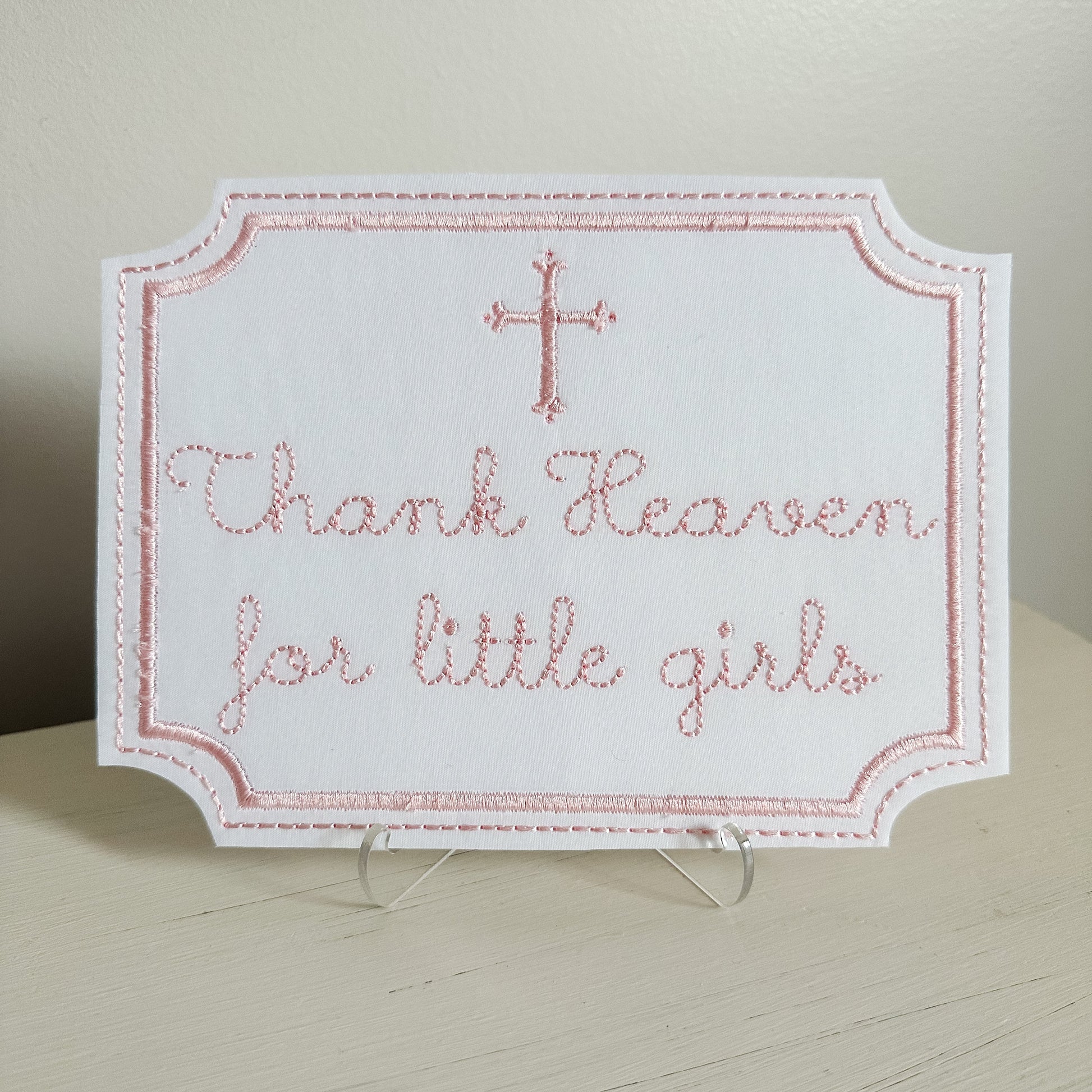 Embroidered sign with 'Thank Heaven for little girls' text on a stand.