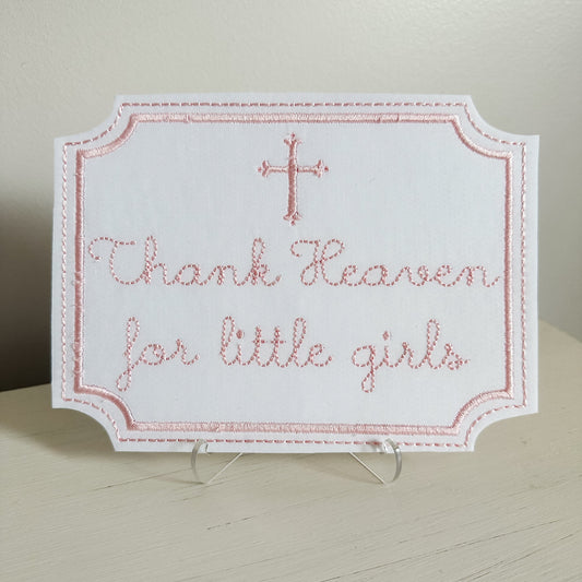 Embroidered sign with 'Thank Heaven for little girls' text on a stand.