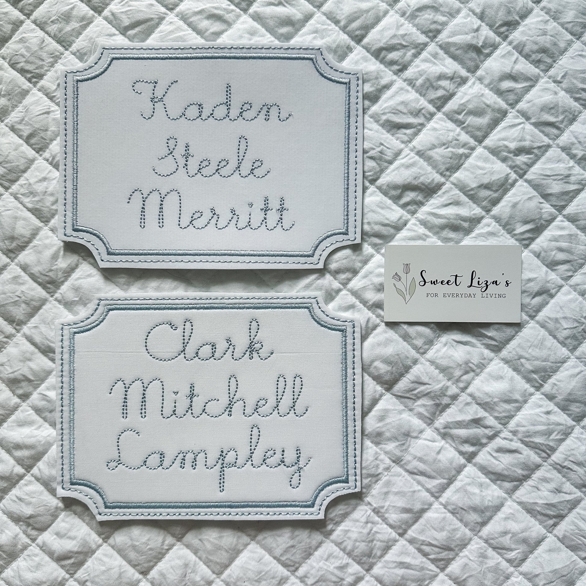 Two embroidered nameplates on a quilted fabric background with 'Sweet Liza's' branding.